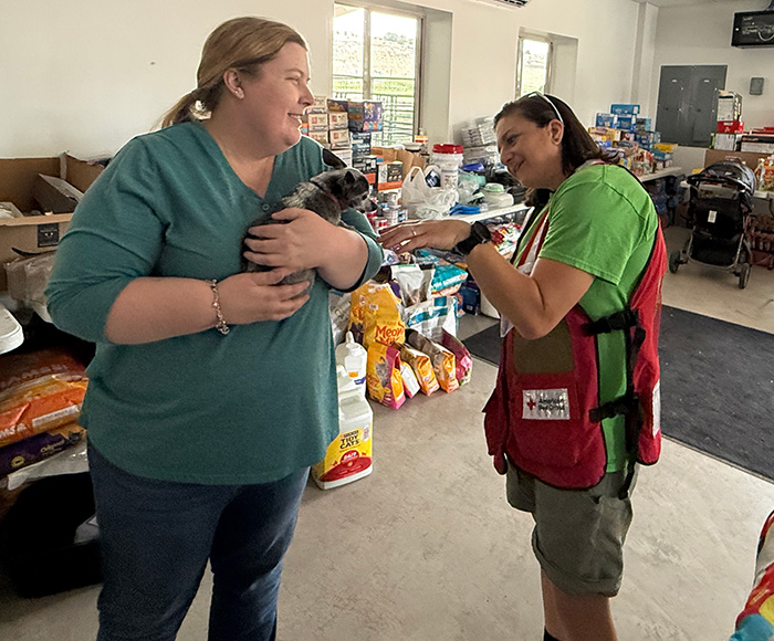 A Red Cross volunteer and woman look after a dog inside of a pet shelter