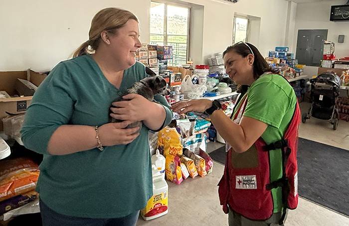 A Red Cross volunteer and woman look after a dog inside of a pet shelter