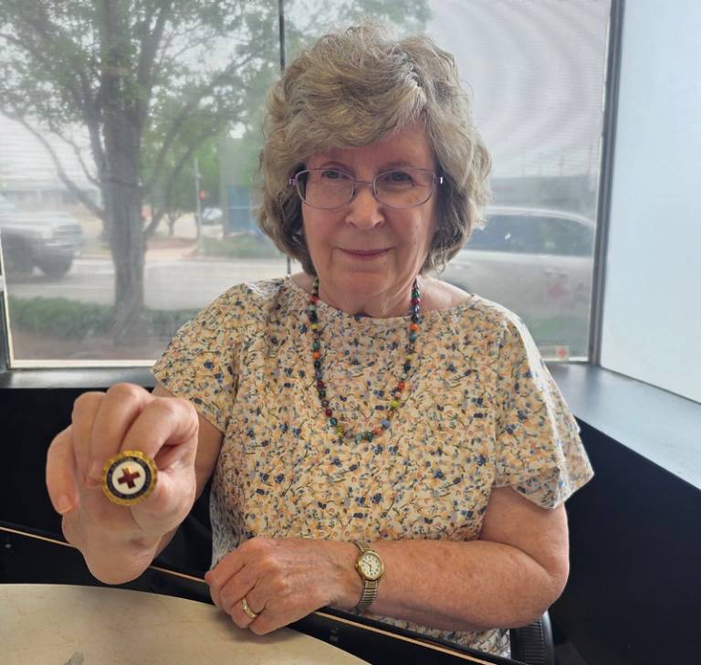 A woman, seated, holding a Red Cross pin
