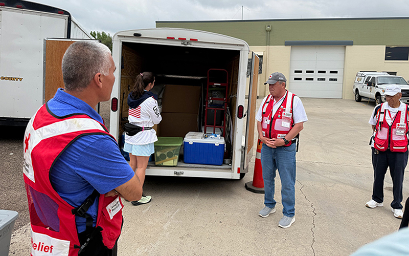 Several Red Cross volunteers and visitors look at a Red Cross-branded trailer with equipment inside