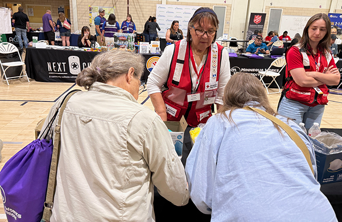 A Red Cross volunteer in a discussion with two women at a table inside of a packed gymnasium