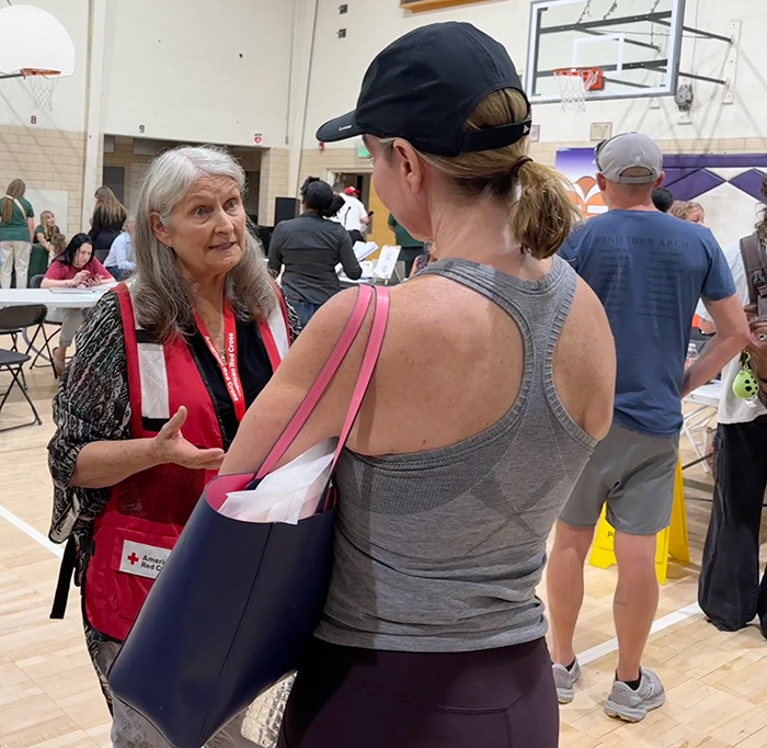 A Red Cross volunteer in a discussion with a woman inside of a packed gymnasium