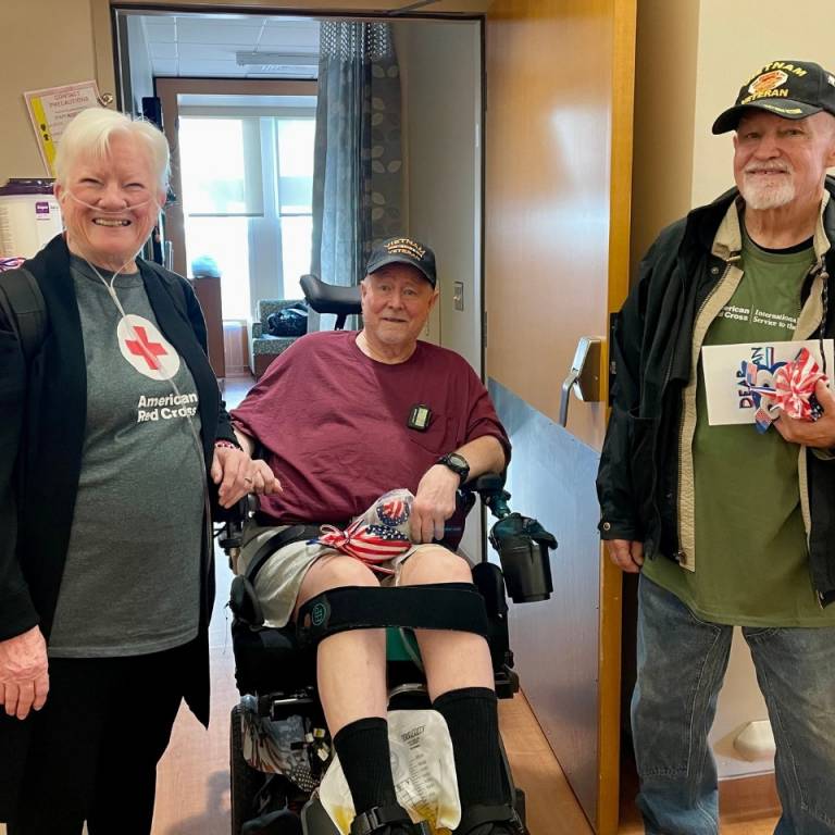 Two Red Cross volunteers stand with a veteran using a wheelchair.
