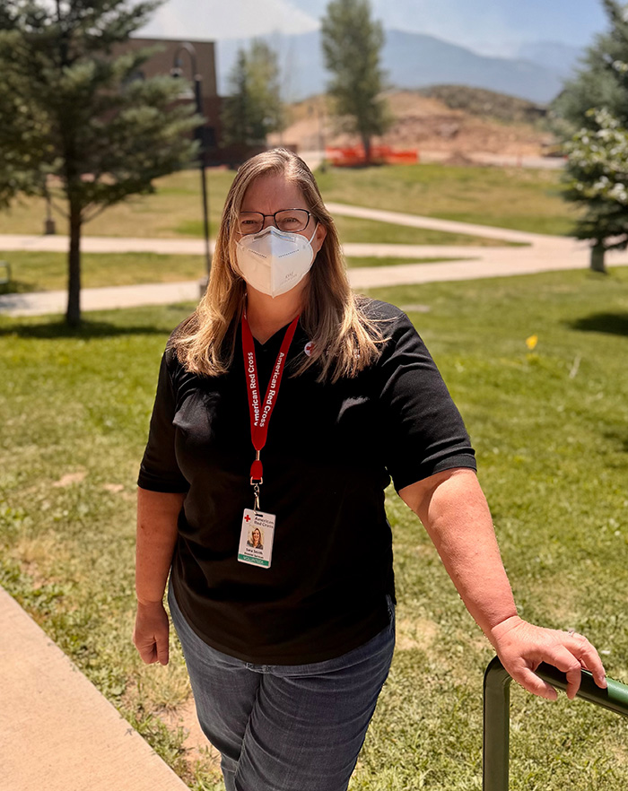 A Red Cross volunteer wearing a mask stands outside next to stairs