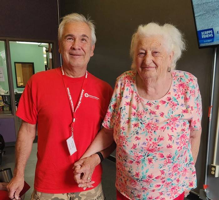 A Red Cross volunteer in a red shirt stands next to an older woman with a pink shirt.