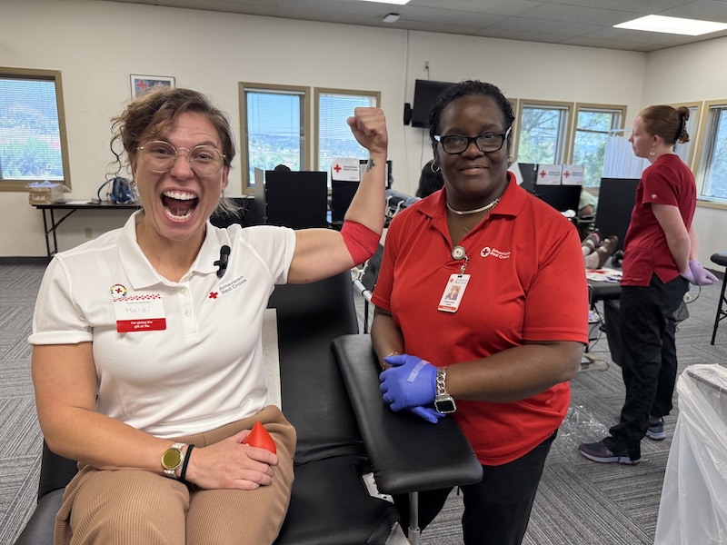A woman flexes after donating blood, with a Red Cross phlebotomist standing next to her