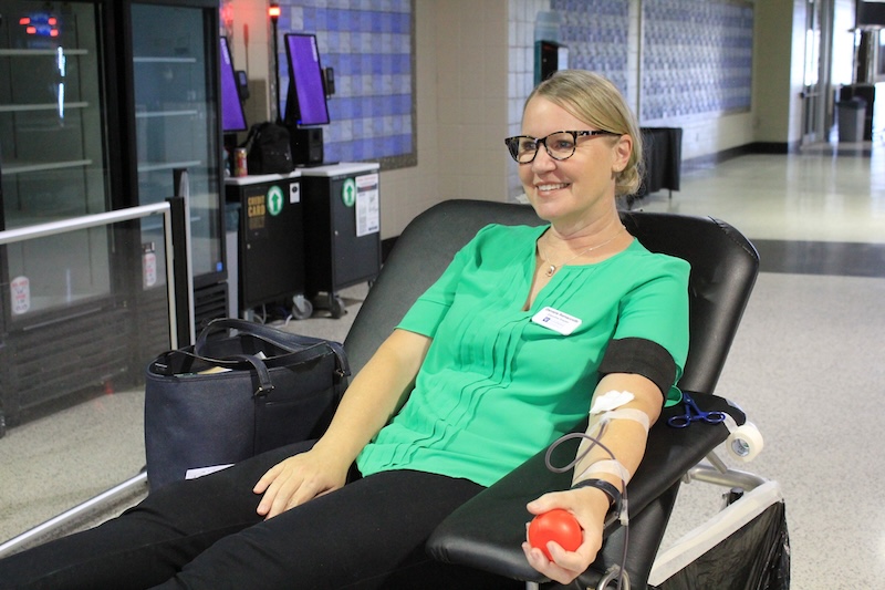 A woman in a green shirt donates blood with a smile on her face