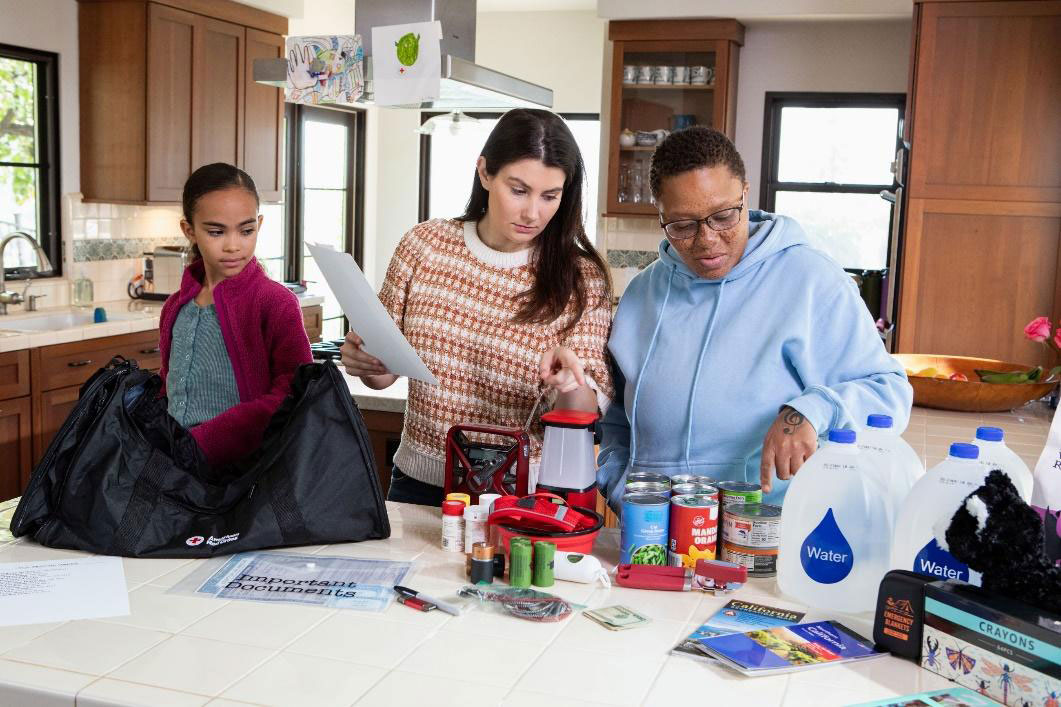 family of three at their kitchen counter with preparedness supplies spread out.
