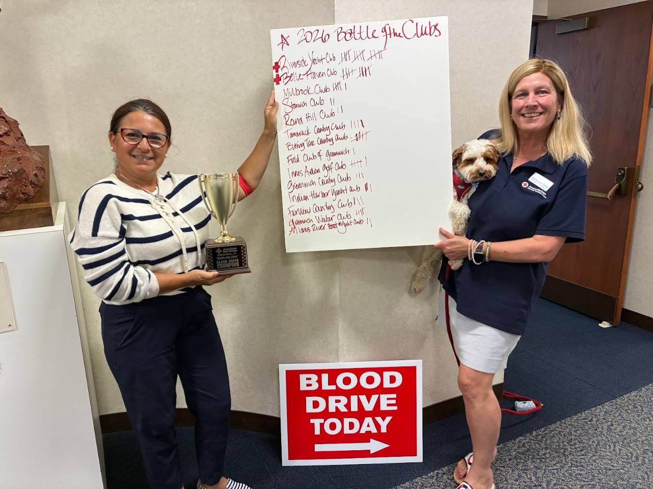 Two people stand in a hallway holding a white sign with red writing on it. 