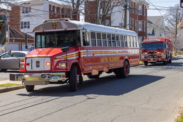 A red fire truck parked on a city street, with buildings and trees lining the road.