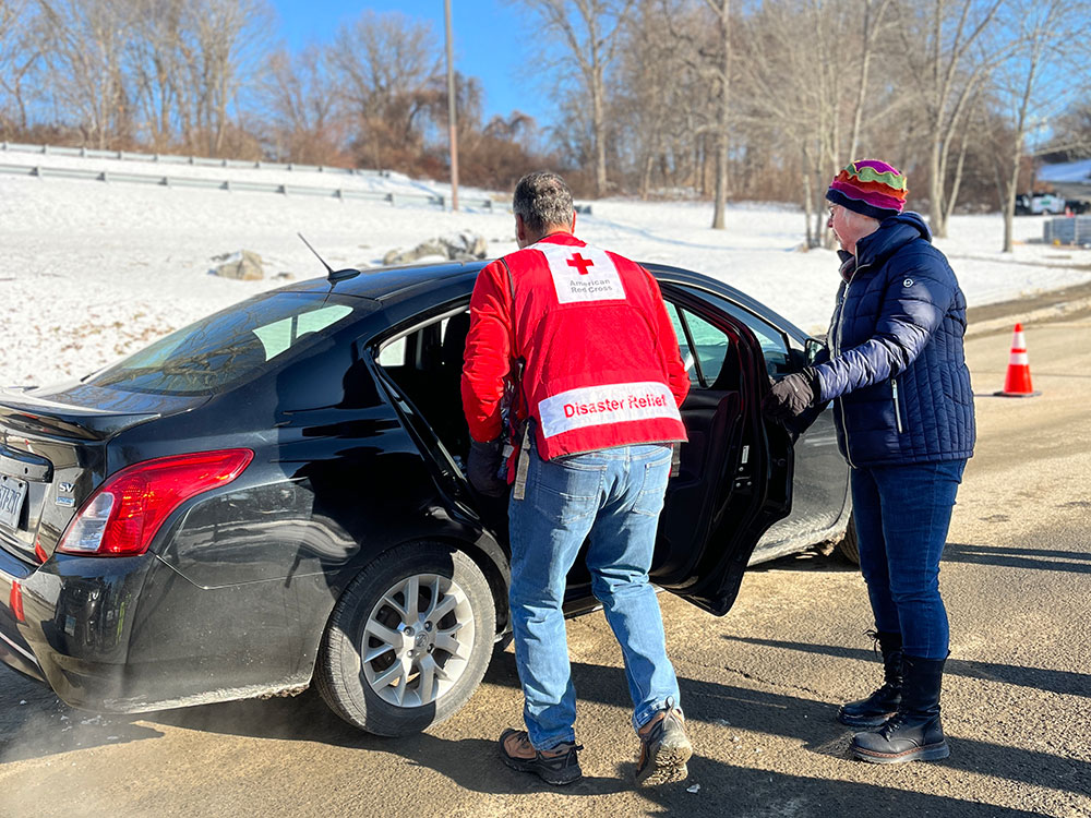 Red Cross volunteer carrying a case of bottled water to a car.