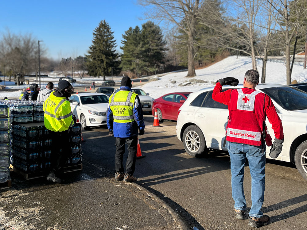 Red Cross volunteers directing traffic in the snow and a stack of bottled water on the side of the road.