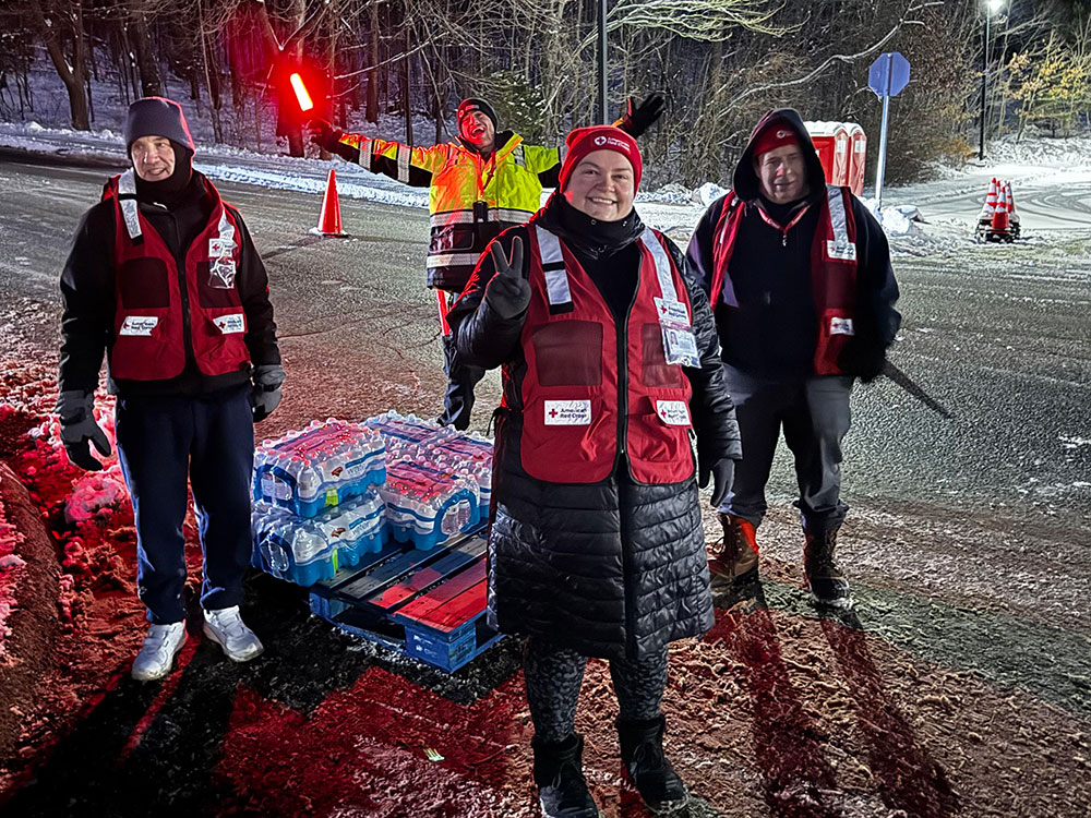 Red Cross volunteers smile for picture while standing next to a stack of bottled water on the side of the road.