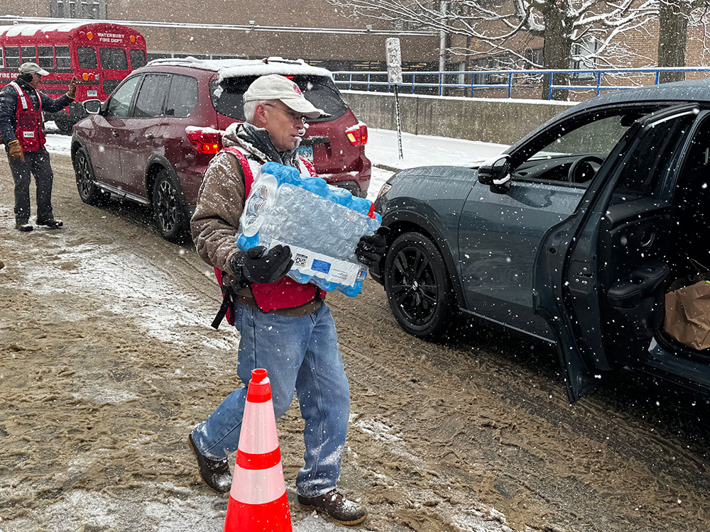Red Cross volunteer carrying a case of bottled water to a car.
