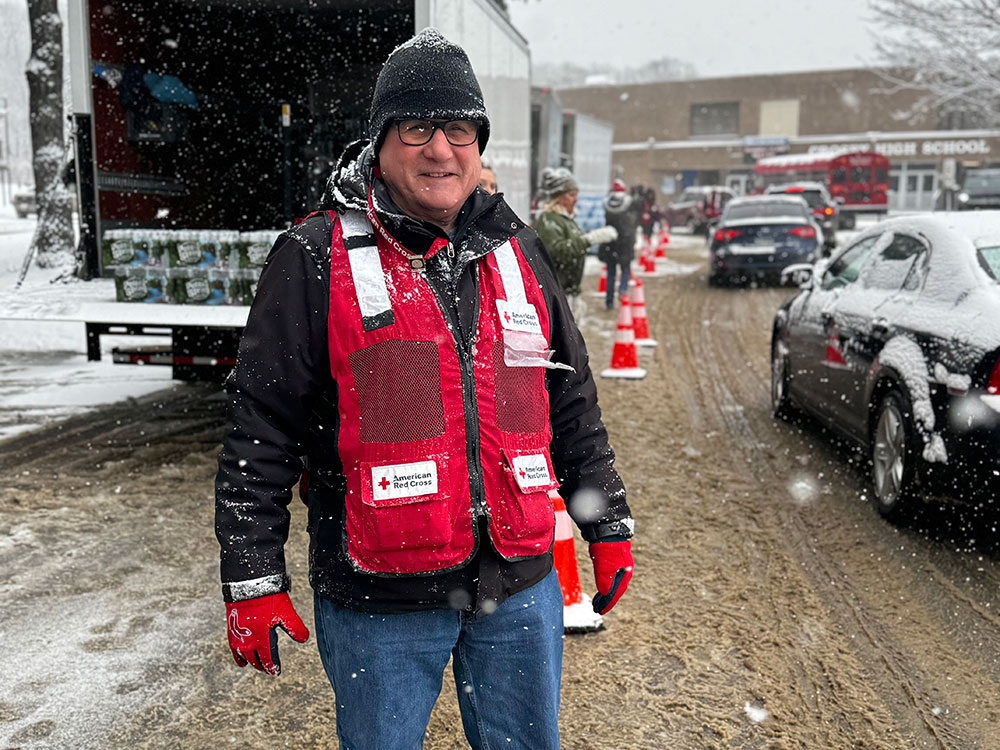 Red Cross volunteer next to truck with bottled water.