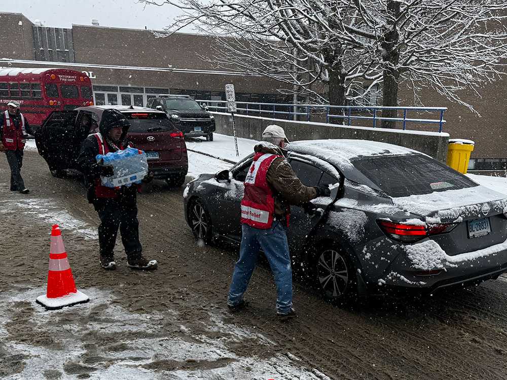 Red Cross volunteer carrying a case of bottled water to a car.
