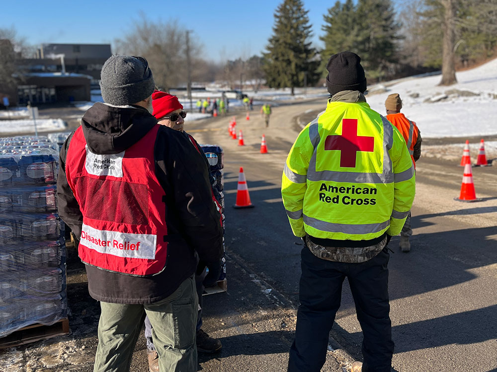 Red Cross volunteers next to a stack of bottled water on the side of the road.
