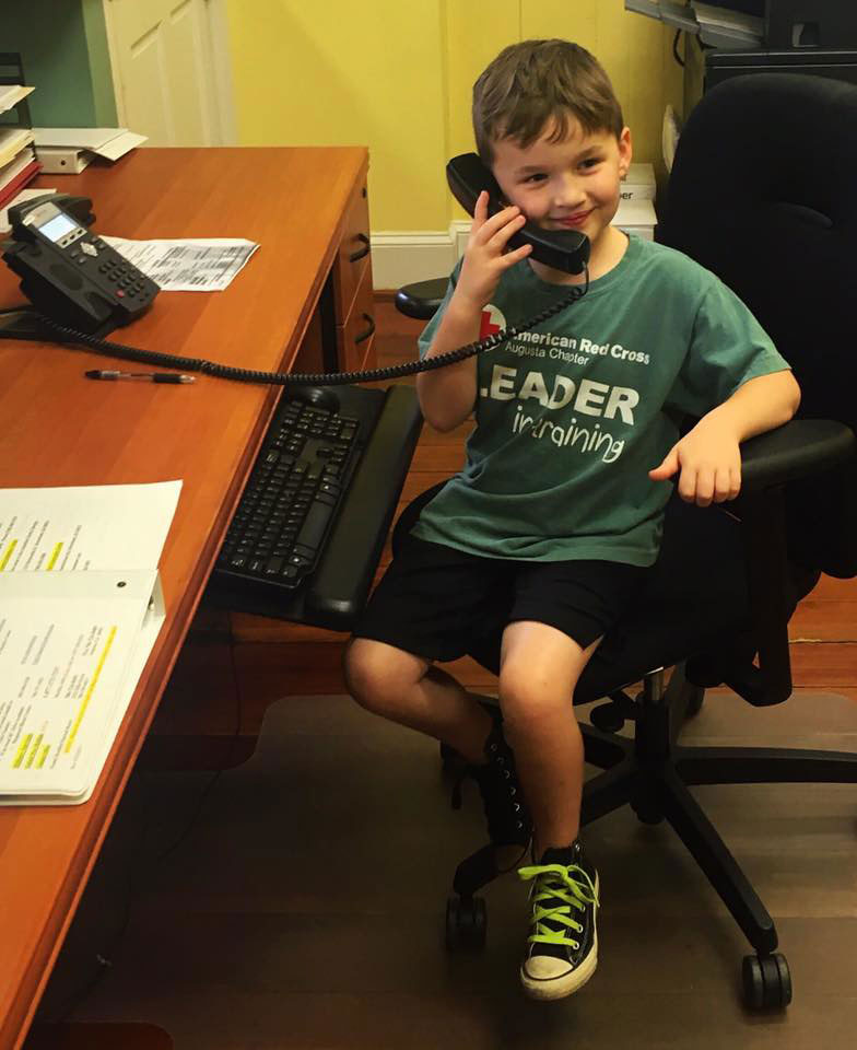 John Leopard sitting in chair at a desk and answering the phone at the Red Cross chapter office.