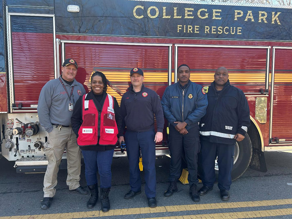 Members of the College Park Fire Department and Red Cross Community Disaster Program Manager Mikkita Dean standing in front of a fire engine.