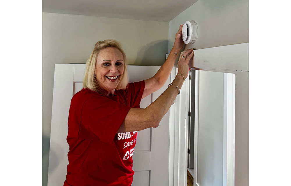 Elizabeth Gill installing a smoke alarm above a door in a home.