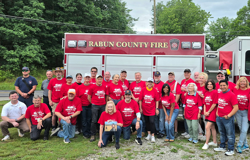 Red Cross volunteers and fire fighters take a group photo in front of a fire engine.