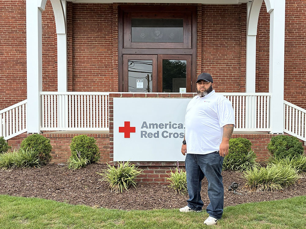 Red Cross staff member Marc Matthews in front of an American Red Cross sign that's in front of a building.