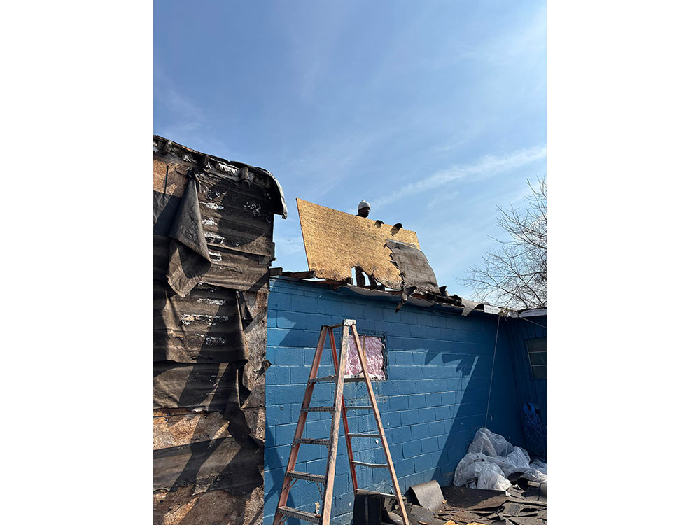 Person standing on roof of a house, lifts an entire section of damaged roof.