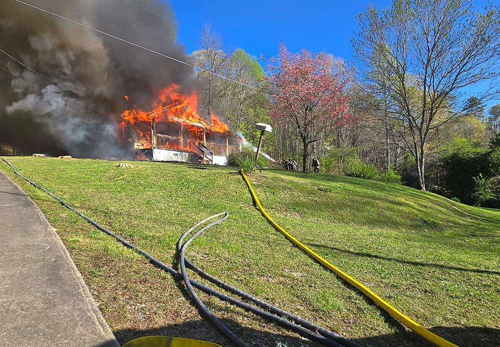 House on fire with fire fighters spraying water on the flames.