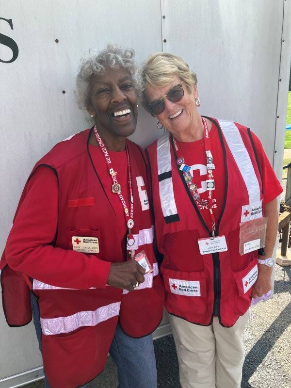 two women in red cross vest smiling standing next to each other