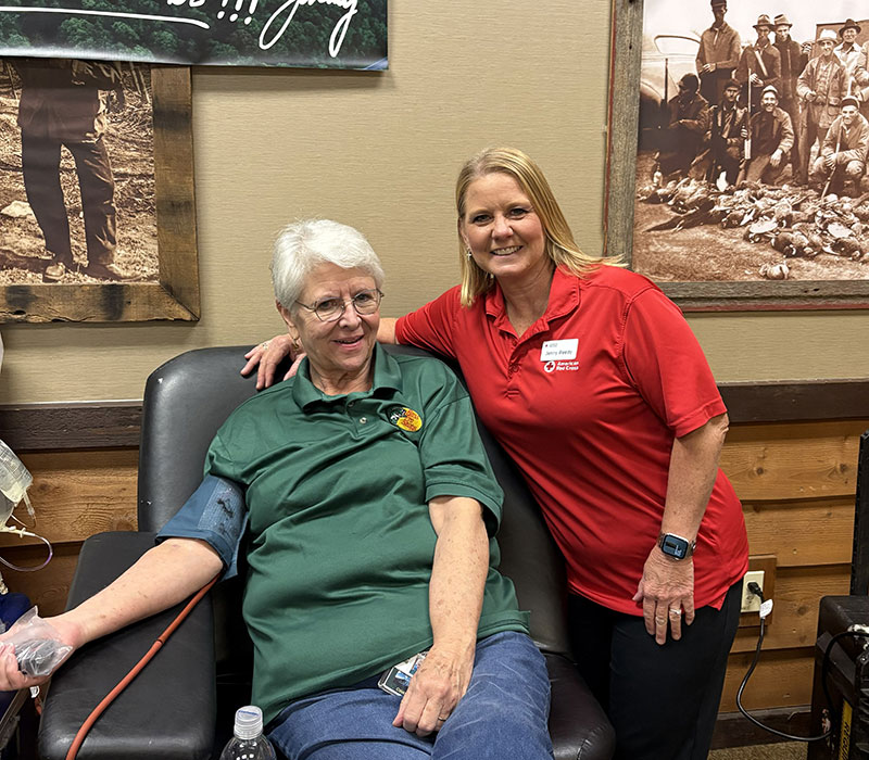 Lis Barton sitting in a chair and donating blood with Red Cross staff member Jenny Reedy standing next to her.
