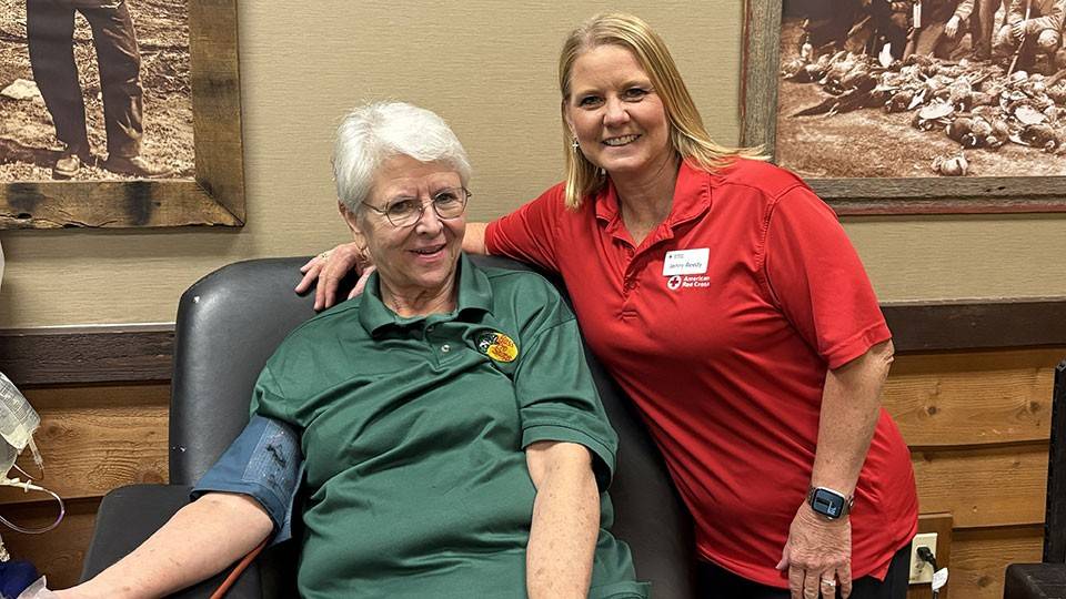 Lis Barton sitting in a chair and donating blood with Red Cross staff member Jenny Reedy standing next to her.