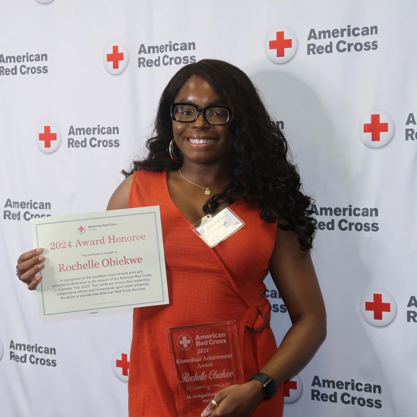 Rochelle Obiekwe wearing glasses and a dress, holds Red Cross awards at event.