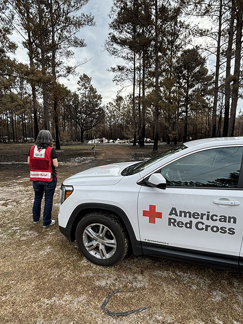 Red Cross Regional Executive Alicia Doherty standing next to a Red Cross vehicle in a wooded area.
