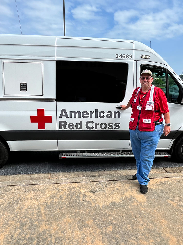 Bill Ladigo wearing a Red Cross hat and vest standing next to a Red Cross van.