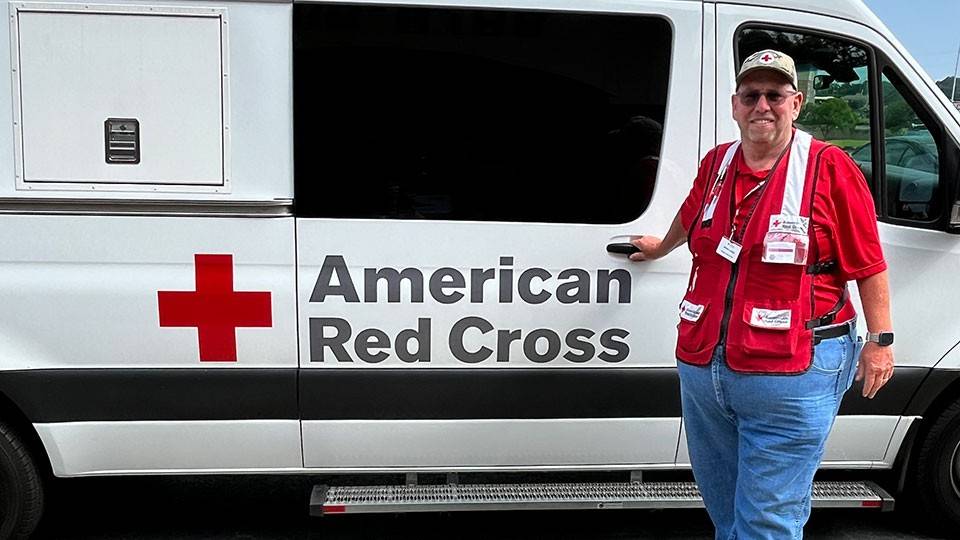 Bill Ladigo wearing a Red Cross hat and vest standing next to a Red Cross van.