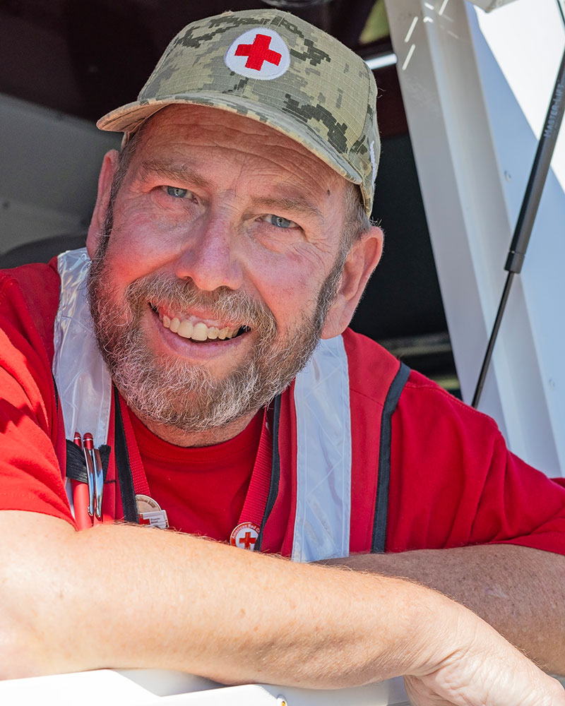 Bill Ladigo wearing a Red Cross hat and vest leaning outside of the Red Cross van open window.