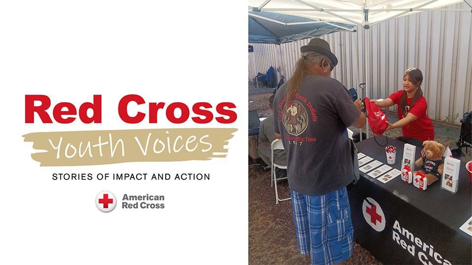Red Cross Youth Voices. A man receives a red bag from a smiling volunteer, Anna Maxwell, at an American Red Cross booth. The table displays pamphlets, pens, and a stuffed toy under a canopy.