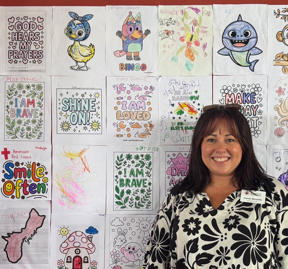 Caedy Minoletti smiling while standing next to a wall covered with colored in childrens drawings.