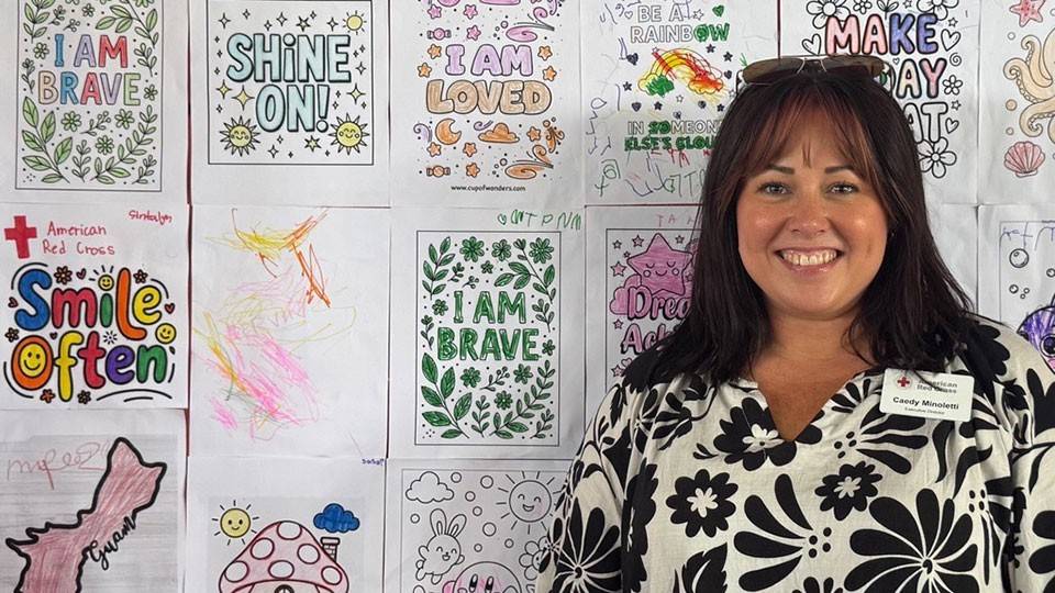 Caedy Minoletti smiling while standing next to a wall covered with colored in childrens drawings.