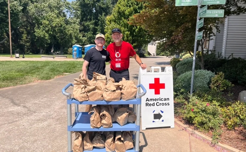 Two Red Cross volunteers standing at a table with supplies.