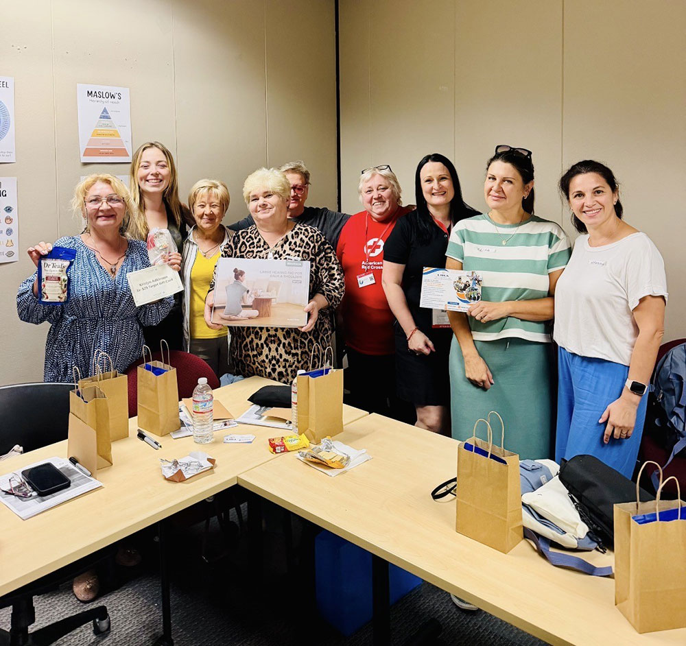 nine Russian-speaking volunteers holding up gift bag items in an office room.