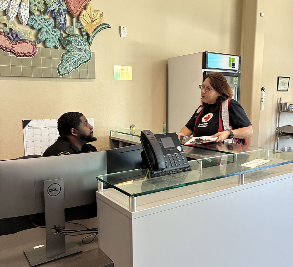 Red Cross volunteer Lora Barrett speaking to a man sitting behind a reception desk in an office.