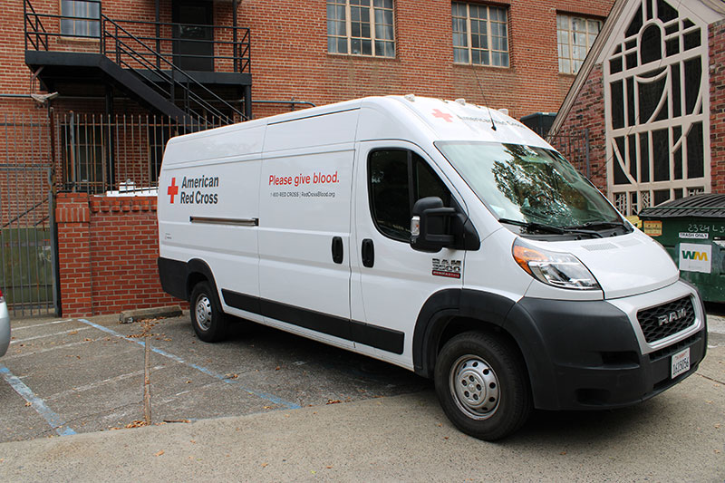 a Red Cross van parked in a parking spot in front of a brick building.