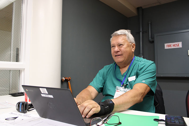 a volunteer sitting behind a table while typing on a laptop.