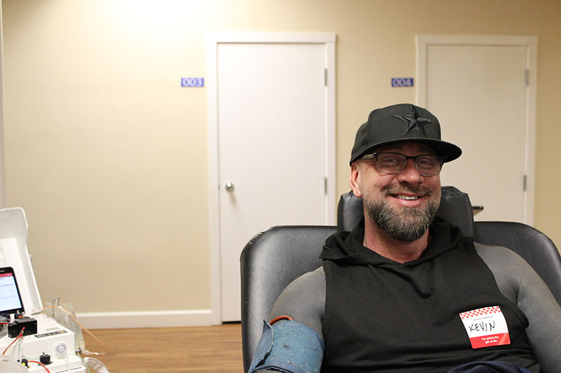 a man, wearing hat and glasses, sitting in a chair and donating blood.
