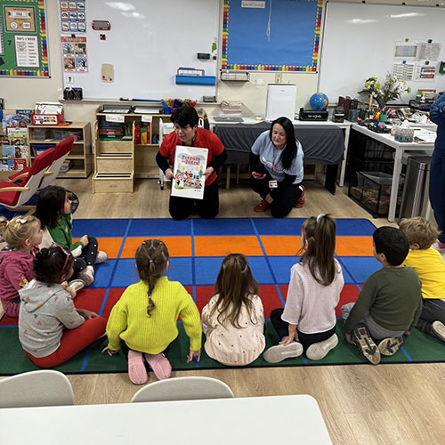 Francis Huezo teaching a class of children that are sitting on a floor mat.