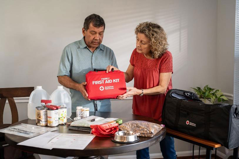 two people holding a Red Cross first aid kit bag with emergency supplies on a table in front of them.