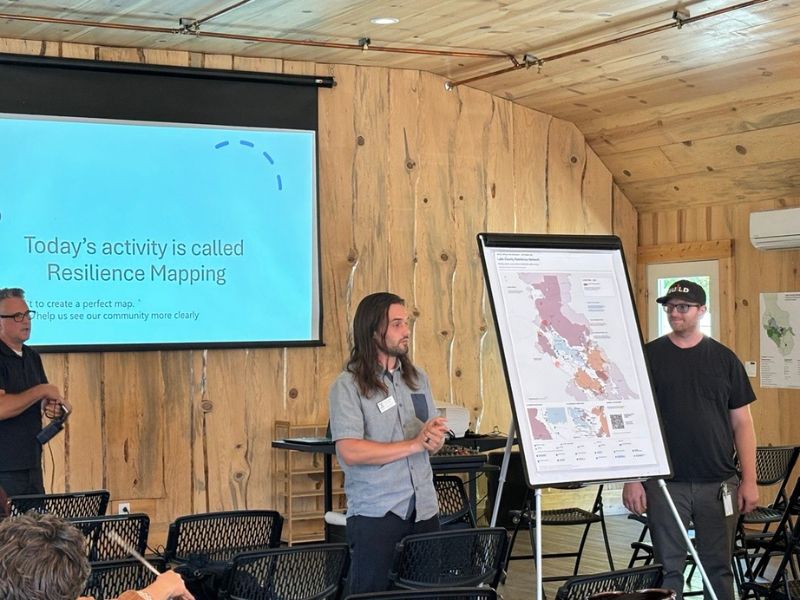 presenters speaking with a board showing a map