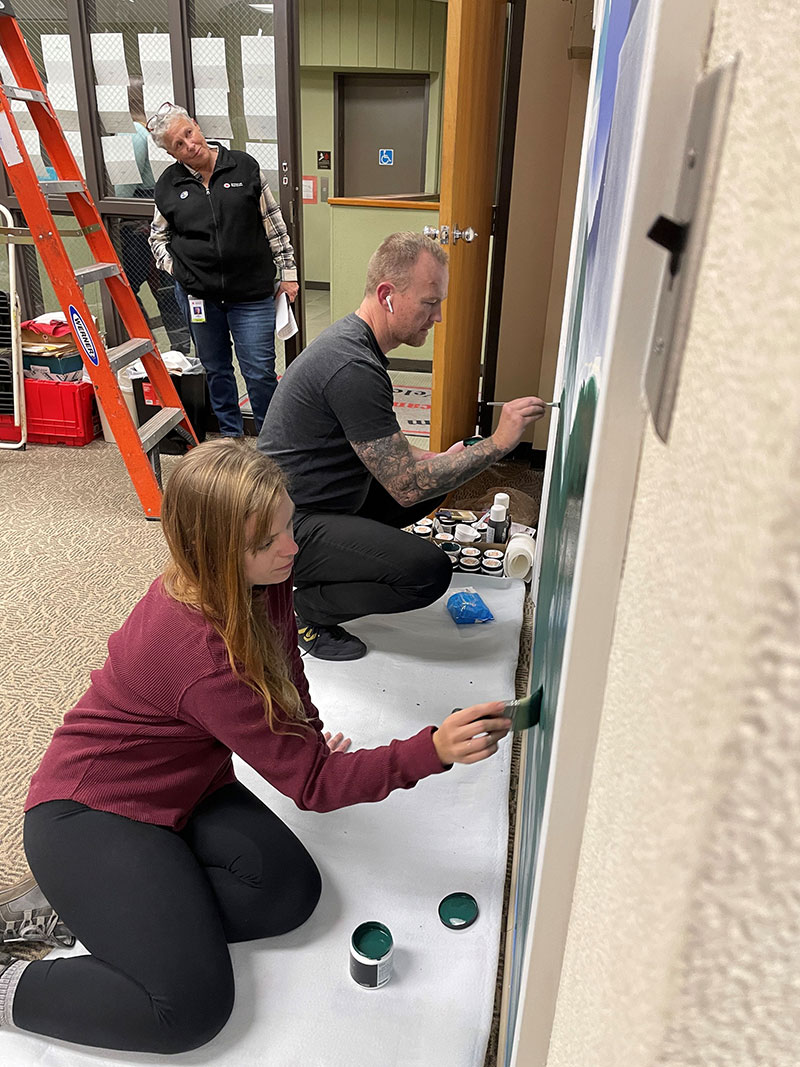 Two people painting a mural with another person watching in the background.