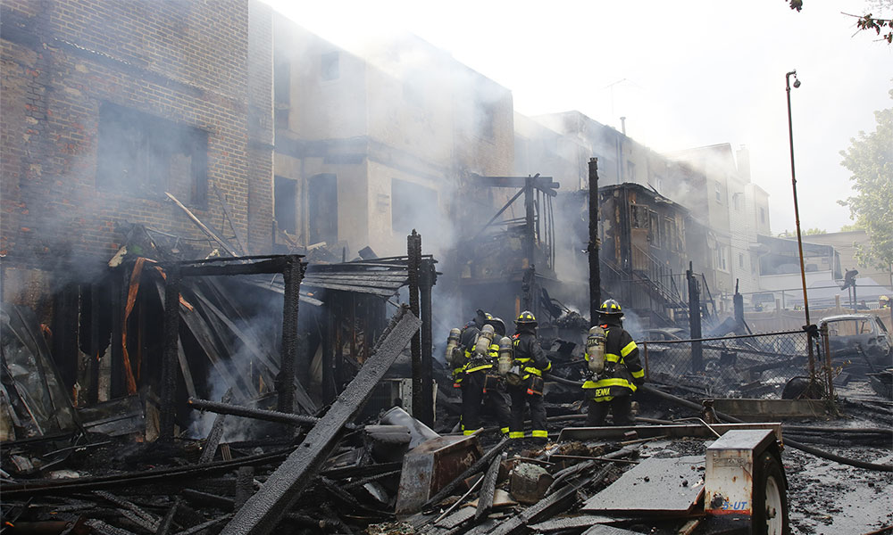 Burned buildings smoking with fire fighters standing in the rubble.